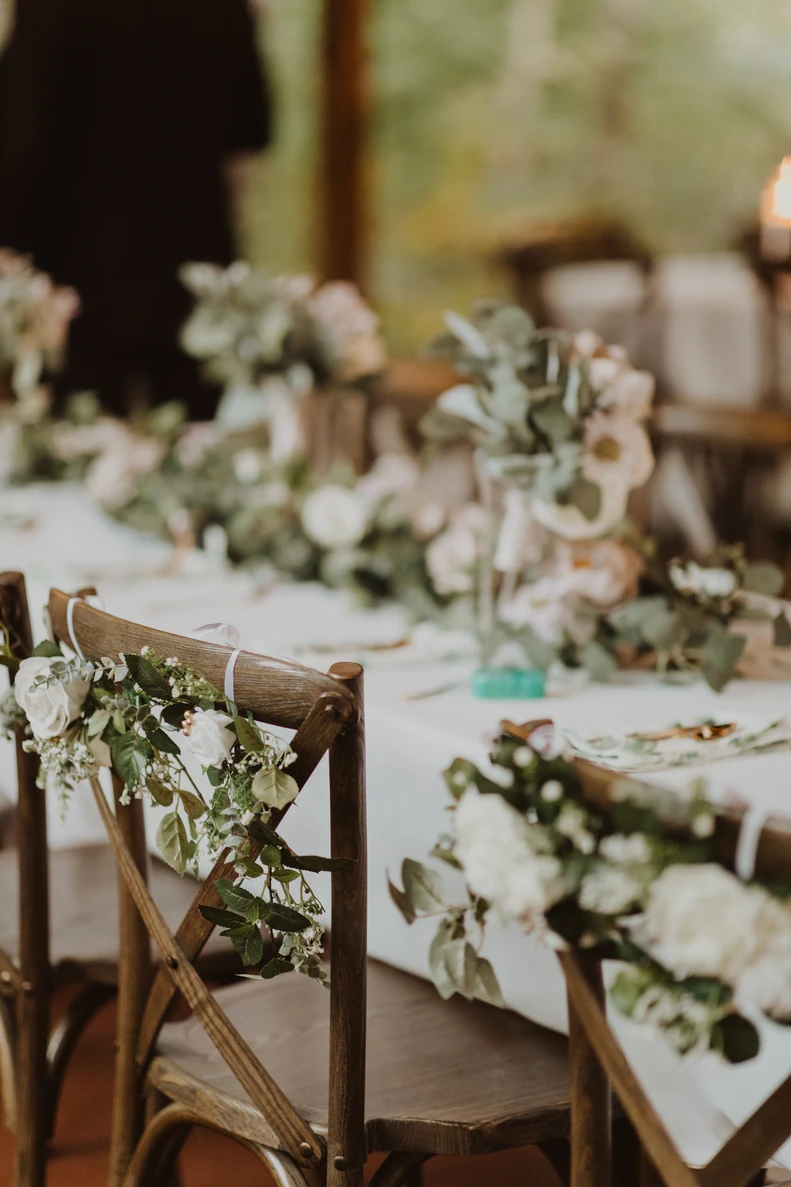 Cross-back chairs and a reception table draped with eucalyptus garland and white florals.